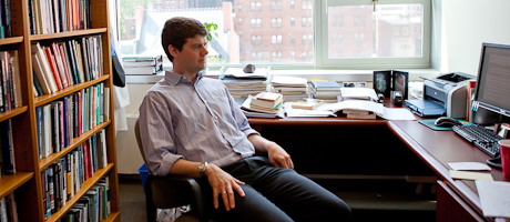 John Sides sits in office in front of desk with stacks of books behind him in shelves