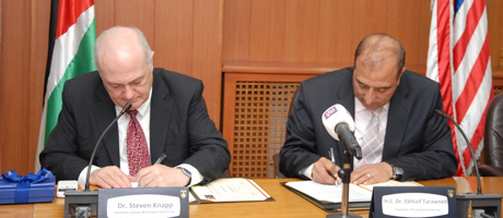 Steven Knapp and Ekhleif Tarawneh sit at table and sign document 