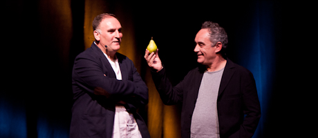 Chefs José Andrés with arms folded and Ferran Adrià holds up pear