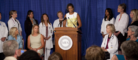 Michelle Obama at podium with Jill Biden, Kathleen Sebelius and others standing behind her