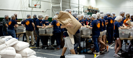 students stuff bags with food in an assembly line in large room
