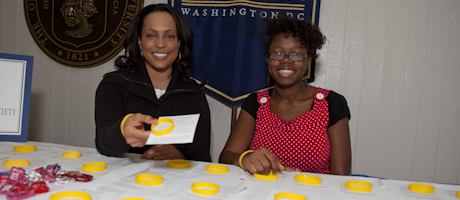 Taara Hassan and Oluwakemi Ajide sit at table organizing cards and yellow bracelets