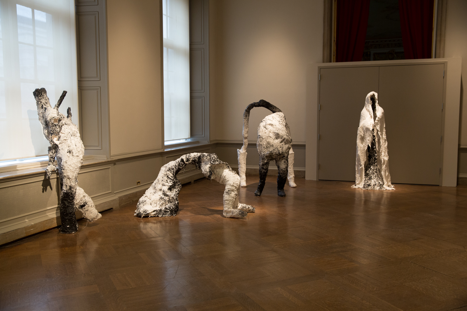 Life-sized, humainoid statues, shrouded in white stand in a row.