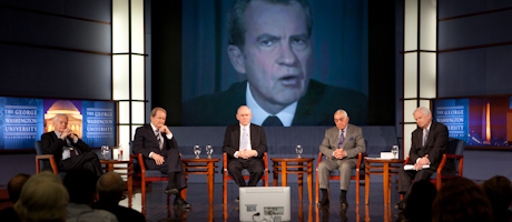 Pat Buchanan, William Gavin, Kenneth Khachigian and Raymond Price sit talking while an image of Richard Nixon appears behind the
