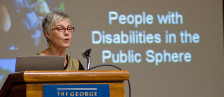 Rosemarie Garland Thompson speaks at podium, "People with Disabilities in the Public Sphere" projected on screen behind her.
