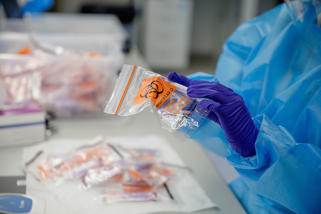 Lab technician handles COVID-19 test sample in a bag.