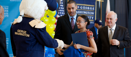 student shaking mascot George's hand when she is awarded SJT scholarship with her family and President Knapp looking omn