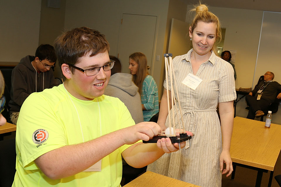 Prof. Megan Leftwich looks on, as a smiling student uses an interactive exhibit at STEM Day.
