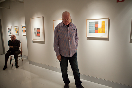 Sean Scully stands in Luther Brady gallery with his art work on walls on display, as Luther Brady sits in background
