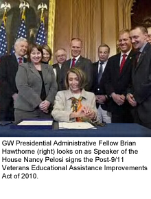 group of men and women in suits, including Brian Hawthorne, look on as Nancy Pelosi signs bill