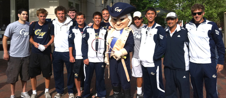 members of GW men's tennis team smile with mascot George wearing warmup Colonials attire