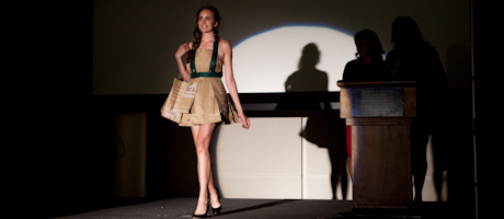 female walks down catwalk in trashion show wearing outfit made out of paper shopping bags