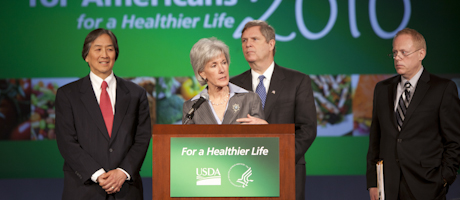 Kathleen Sebelius speaks at a For a Healthier America podium with Howard Koh, om Vilsack and Robert C. Post behind her
