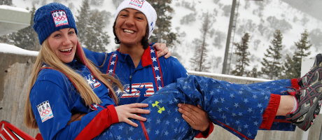 smiling Elana Meyers holds up bobsled teammate in Olympic uniform