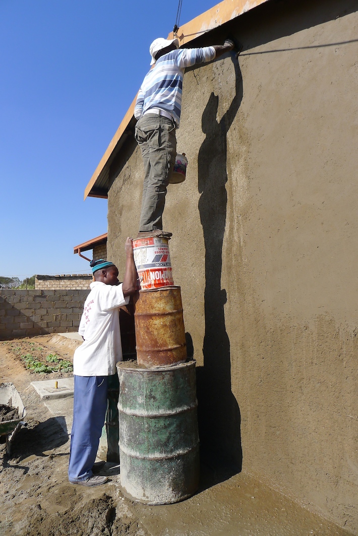 Bokamoso staff apply plaster to a wall to get it ready for mural painting.