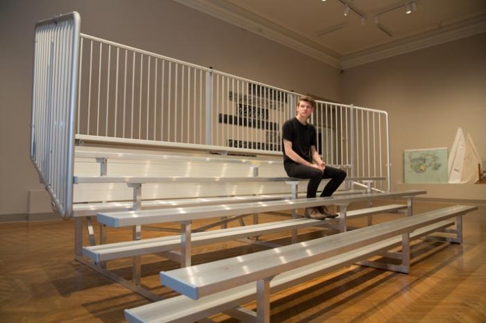 Senior Eliot Hicks, sits on the bleachers of his installation, "Versus."