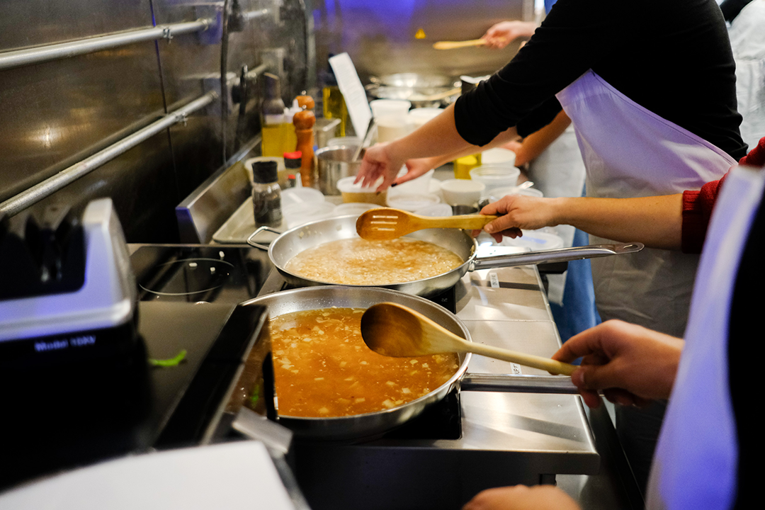 Several students cooking at an oven.