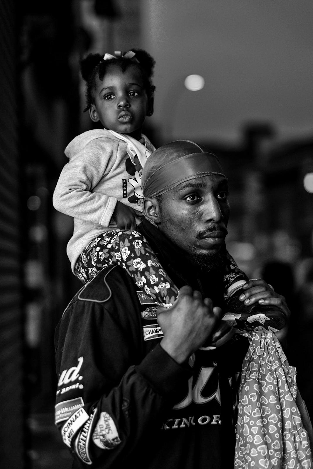 Black and white photo, a father carries his daughter on his shoulders