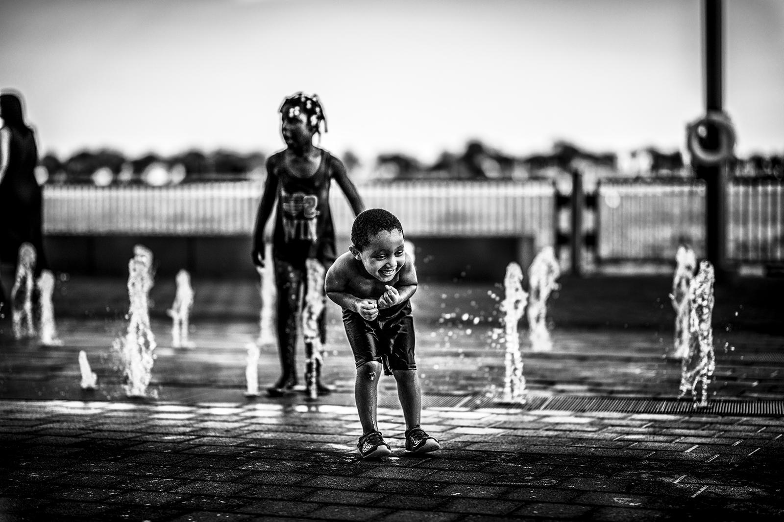 Black and white photo, a delighted child plays in a fountain