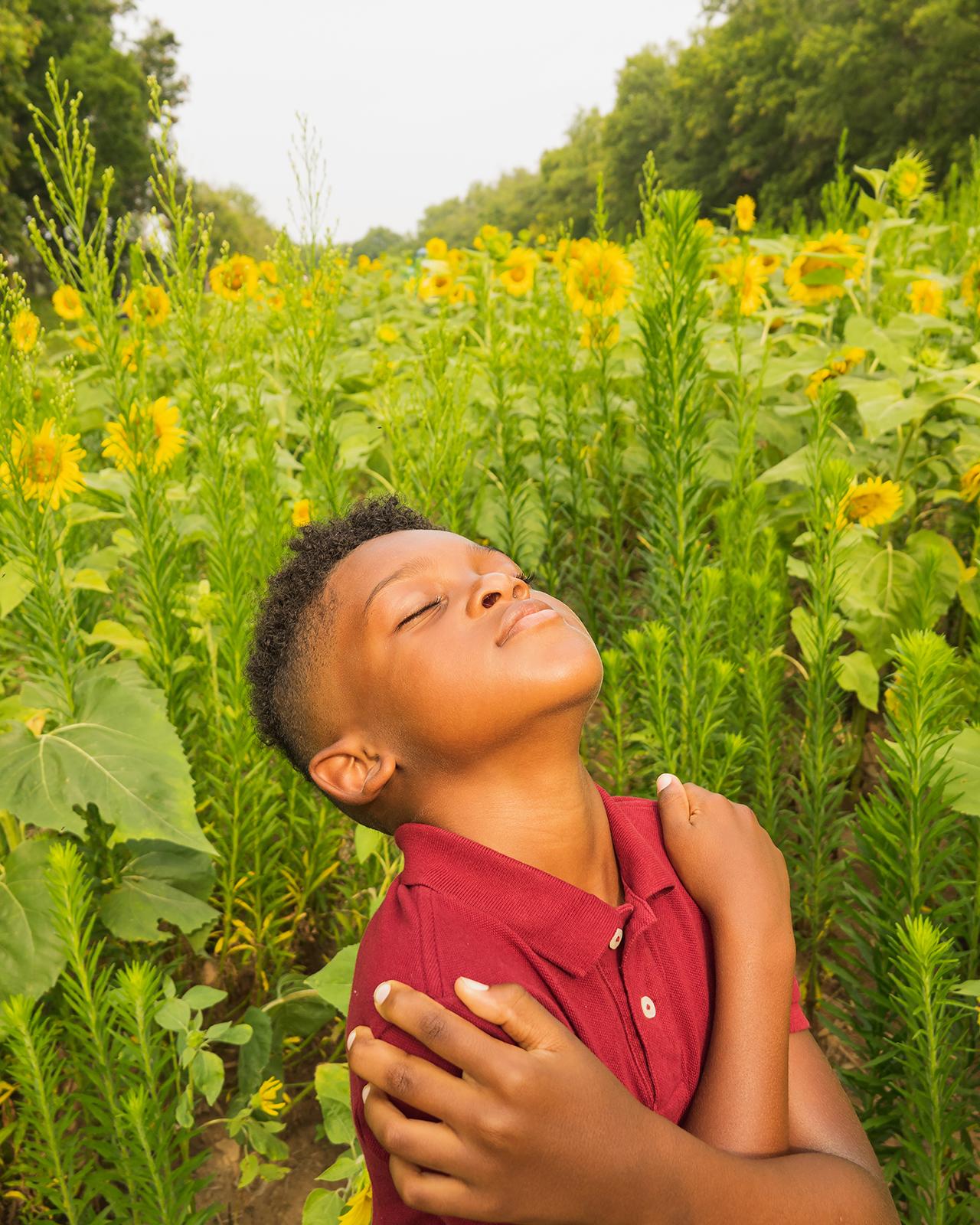 Color photo, a young child lifts his face to the sun in a field of flowers