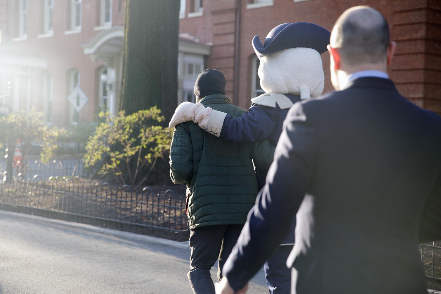 mascot George walks down the street with his arm around a GW community member