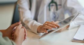 (Adobe Stock image of doctor showing patient information on tablet)