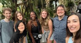 Seven biology students smiling at the camera in front of trees at the Botanic Garden.