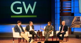 Four people talking on stage with GW logo in background.