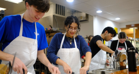 undergraduates Noah Troppe, Leana Kahwash, Krish Sadhwani and Emma Hodgson in aprons and chopping on a counter in in Italian cooking and culture class.