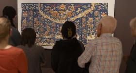 Visitors admire an 18th-century Buddhist priest's silk robe stitched with gold thread at "Intrinsic Beauty." (Lily Speredelozzi/GW Today)