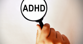 A magnifying glass over the word ADHD & a hand