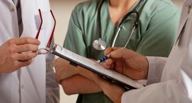 Three people in scrubs consult a medical chart. Their faces are not visible (Adobe Stock)