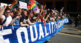 Marching for LGBTQ equality in 2009, marchers wave rainbow flags and carry signs