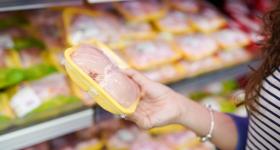 A hand holding packaged raw chicken